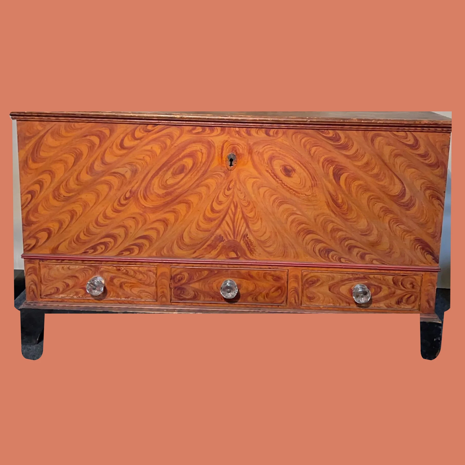 Fancy grain painted chest with decorated front, drawers, and original surface, isolated on a warm salmon background