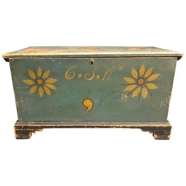 Teal-painted blanket chest with yellow sunflower motifs and visible initials C.S.W., isolated on a white background